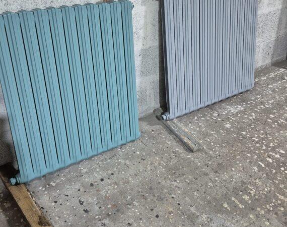 Two ribbed radiators, teal and light gray, propped against a concrete wall in a workshop.